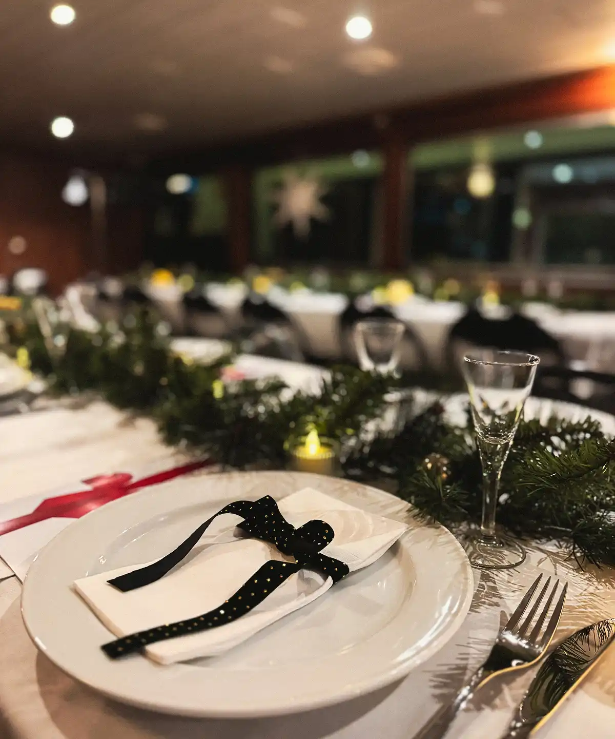 Christmas decorated table with focus on a plate with white napkin and green bow.